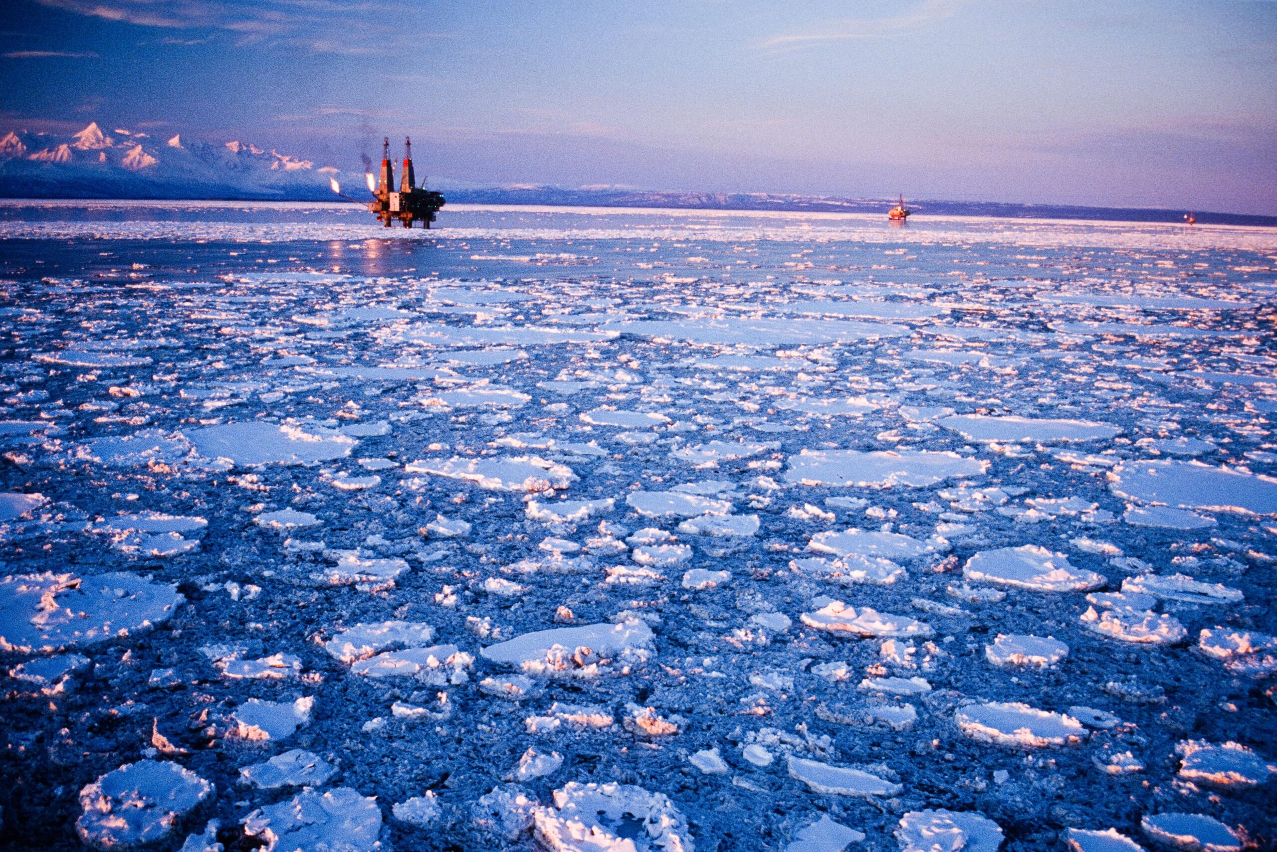 Offshore petroleum drilling rig in icy waters against a blue sky and snowy mountains in the background