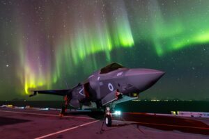 The F-35B lightning on the deck of the HMS Prince of Wales with a display of Aurora Borealis in the background